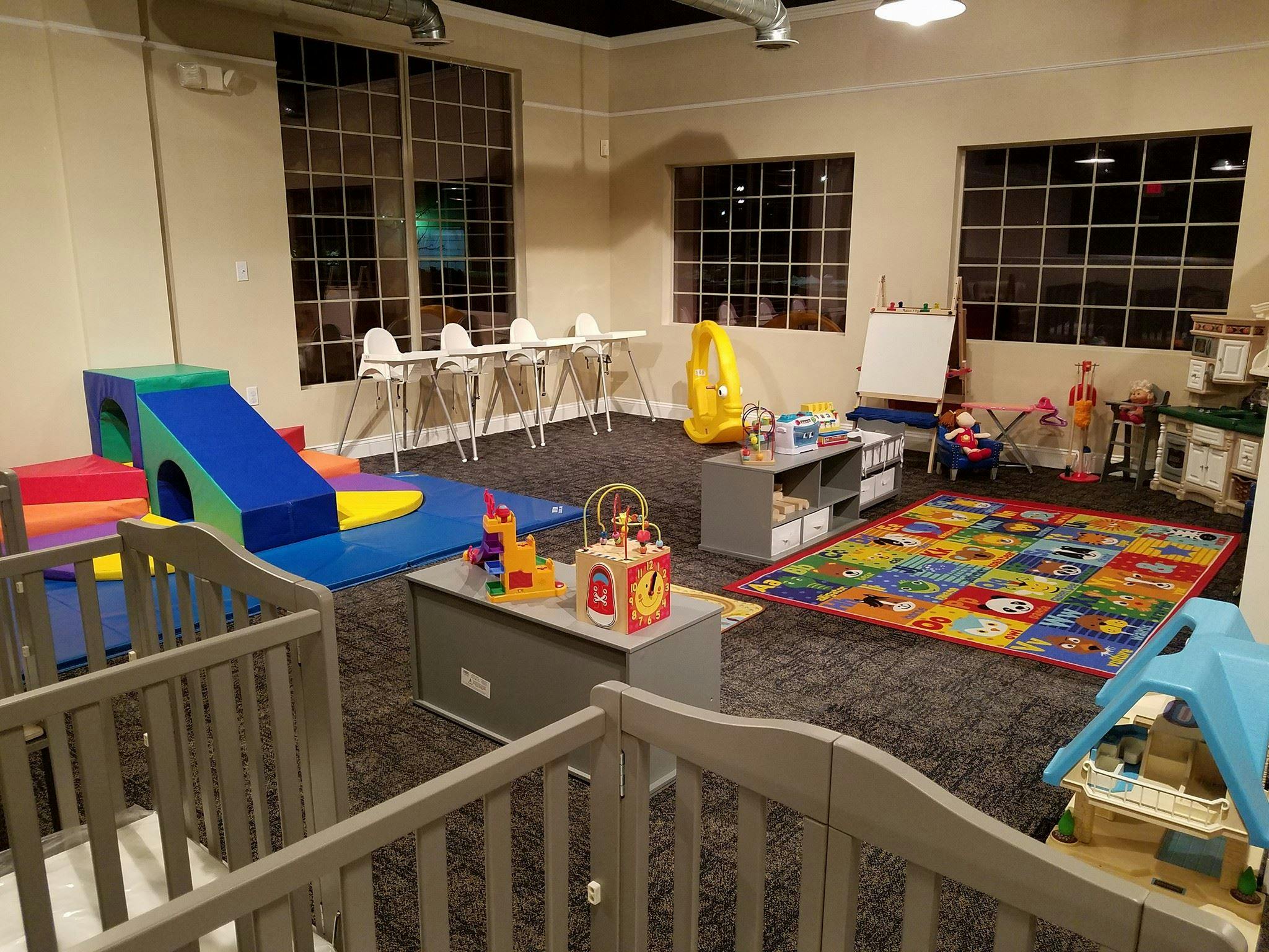 Indoor play area with soft play equipment, cribs, and a colorful rug
