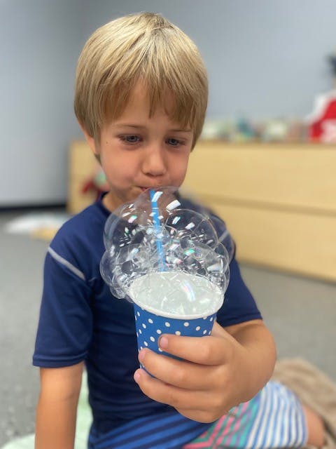 Child blowing bubbles into a cup with a straw