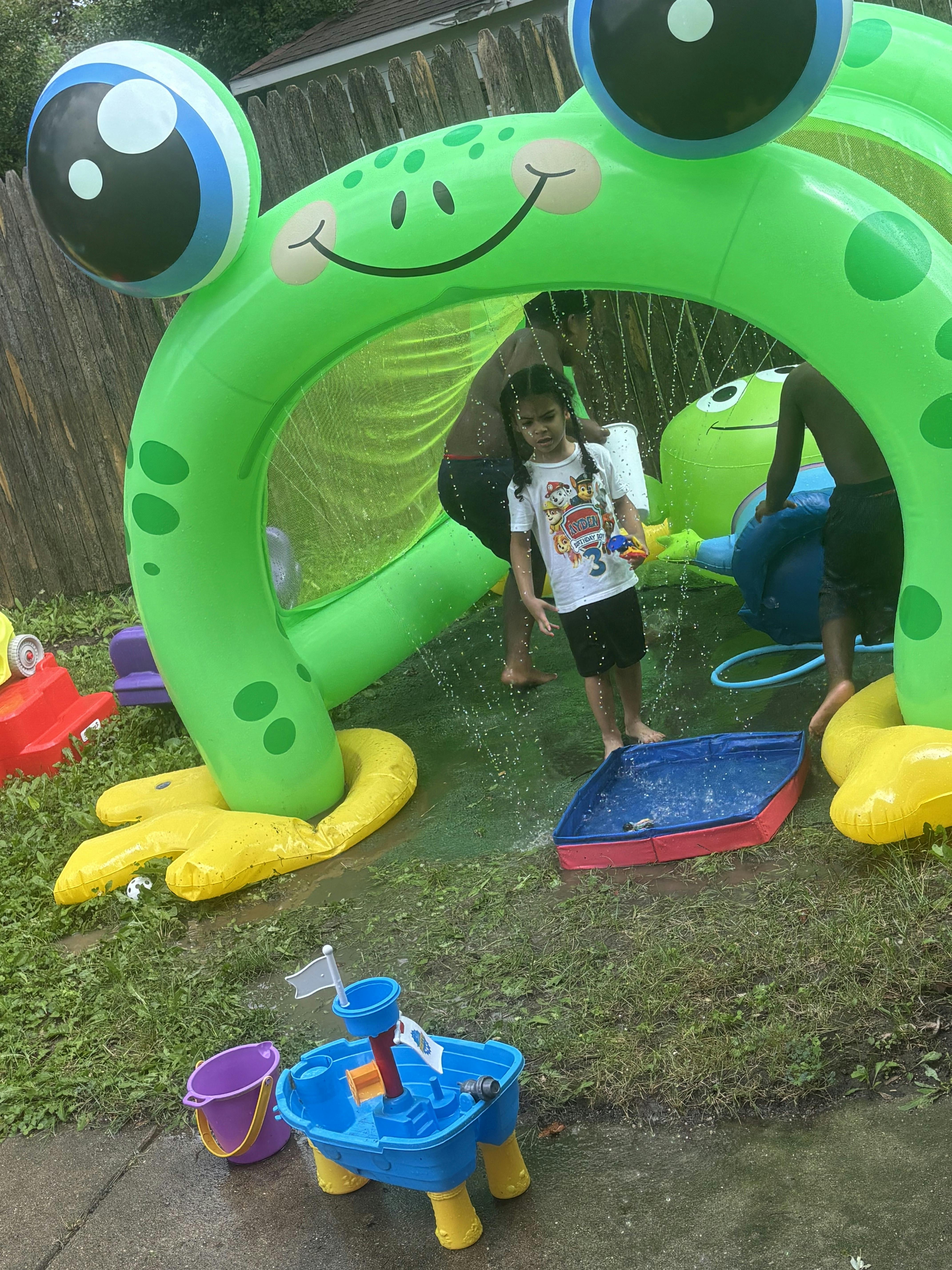 Children playing in water under an inflatable frog sprinkler
