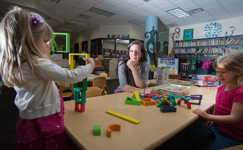 Adult and two children playing with colorful blocks at a table