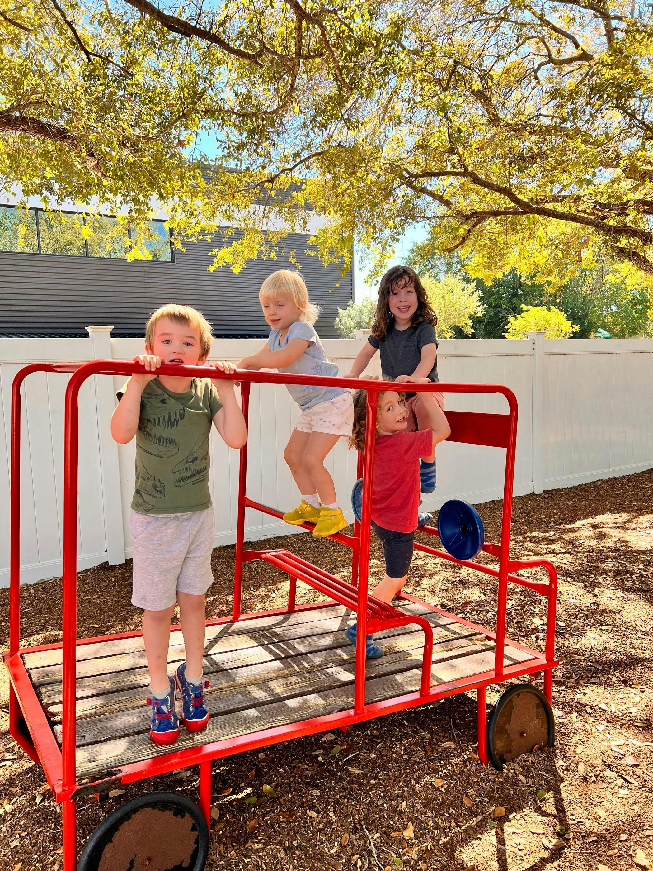 Four children playing on a red metal playground structure under a tree