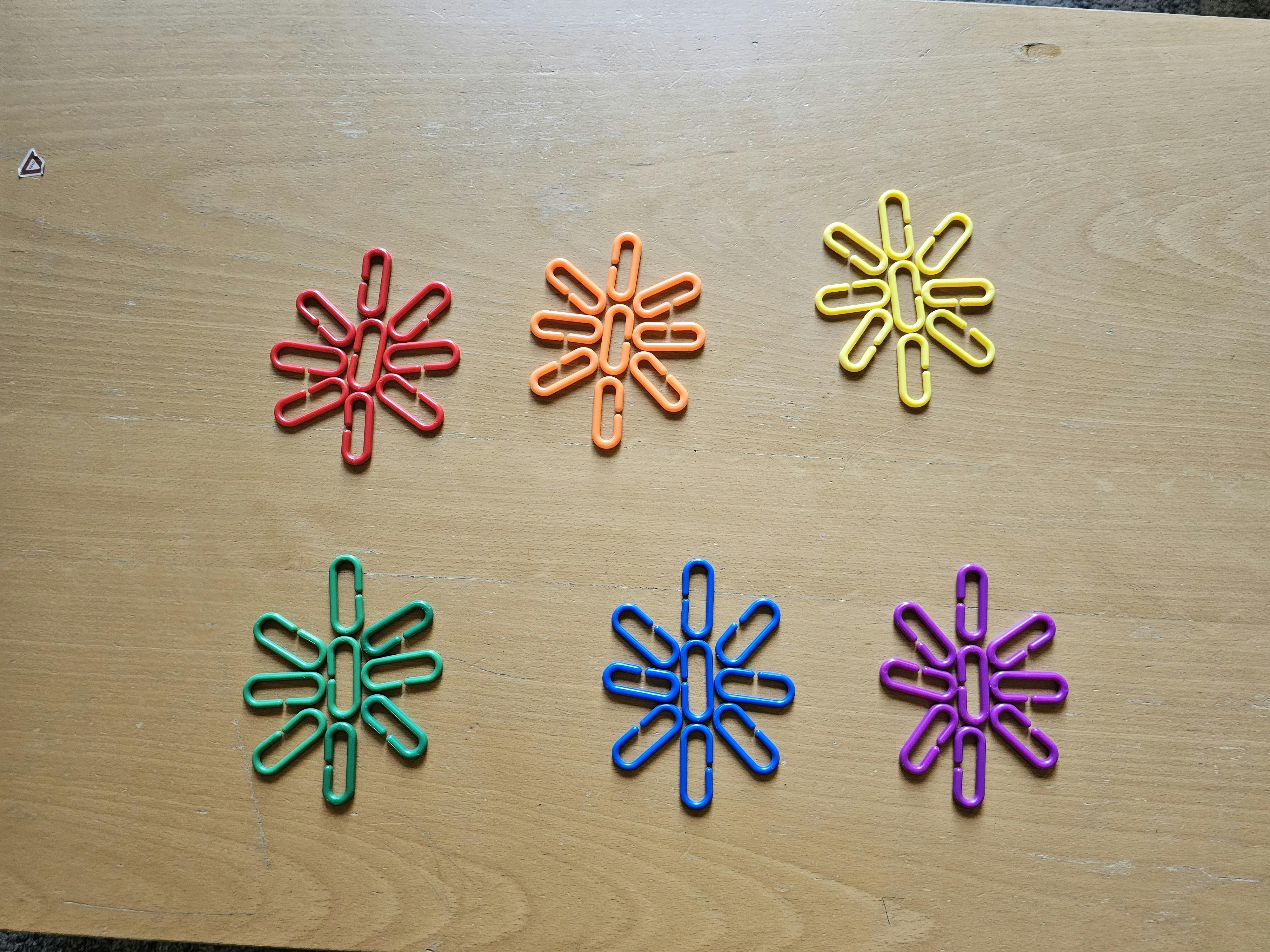 Six snowflake-shaped figures made of plastic links arranged on a wooden surface