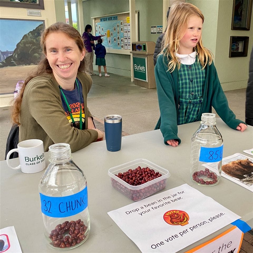 Smiling person and child at a table with jars of beans for voting
