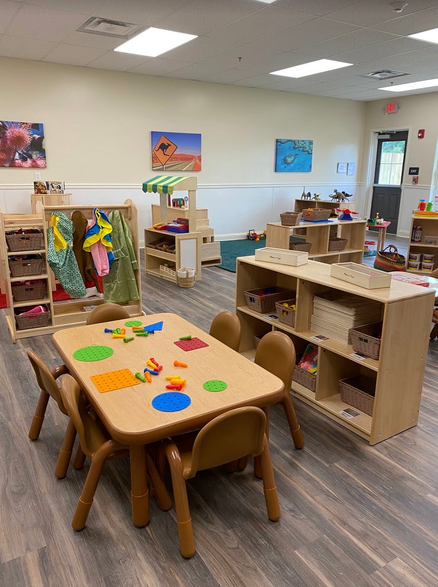 Classroom with small tables and chairs, shelves with toys and supplies