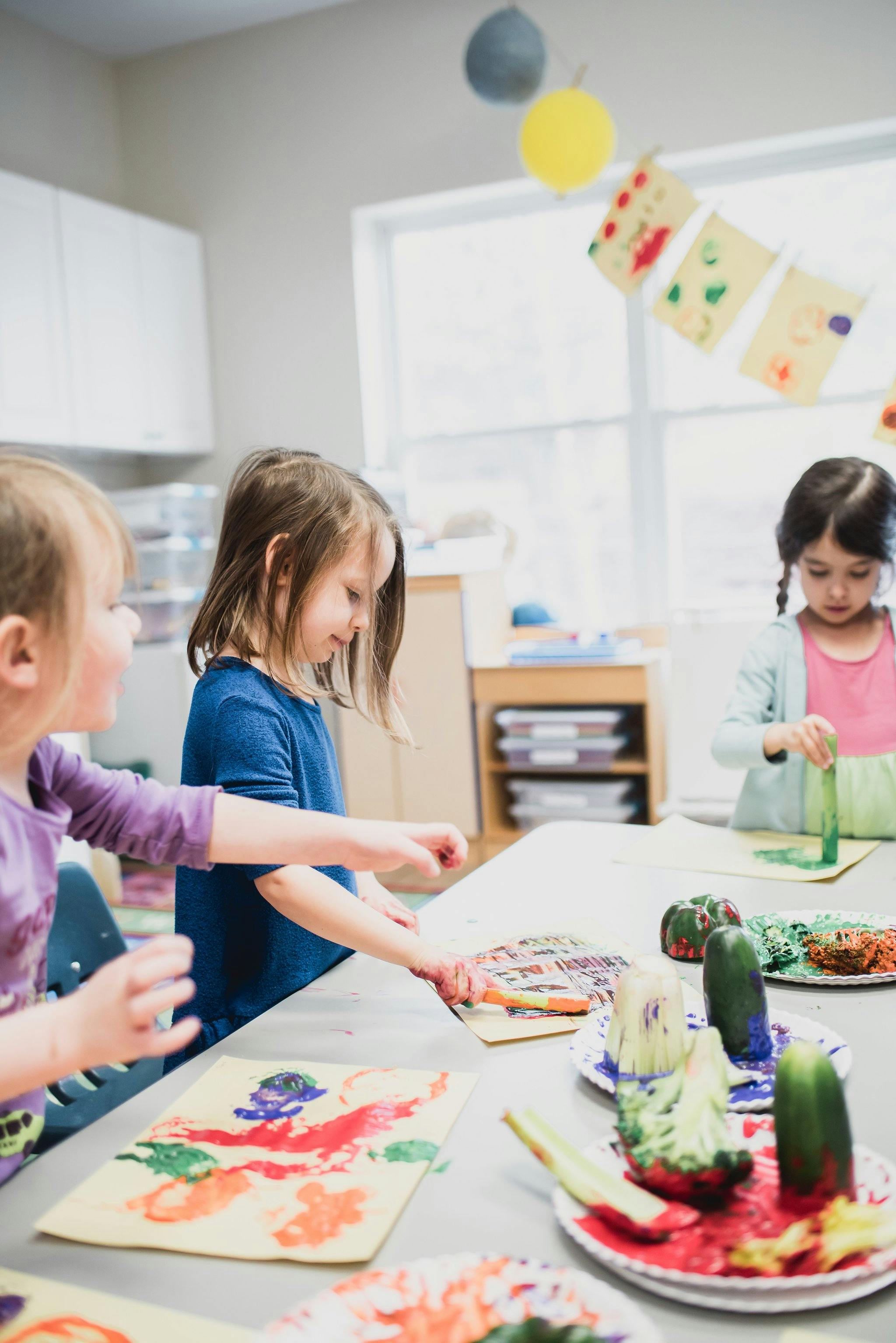 Three children painting at a table in a classroom