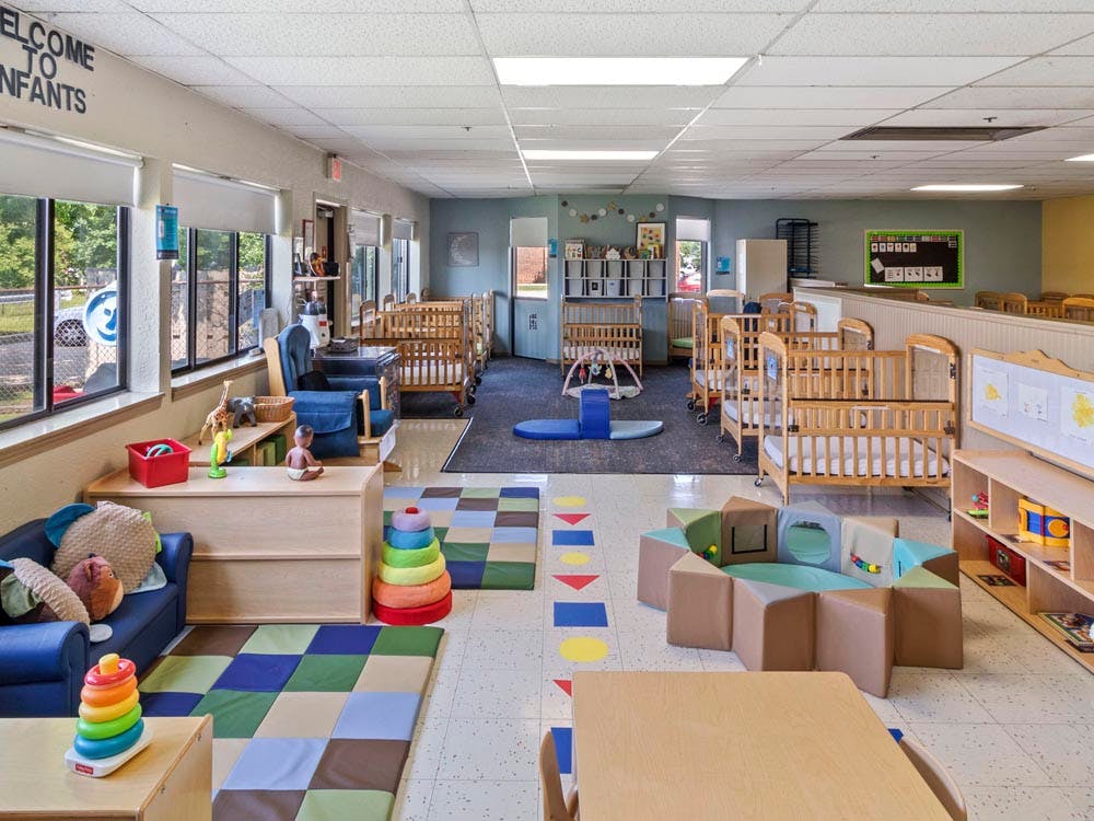 Childcare room with multiple cribs, play mats, and toys