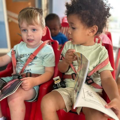 Two children sitting in red chairs, one holding a book
