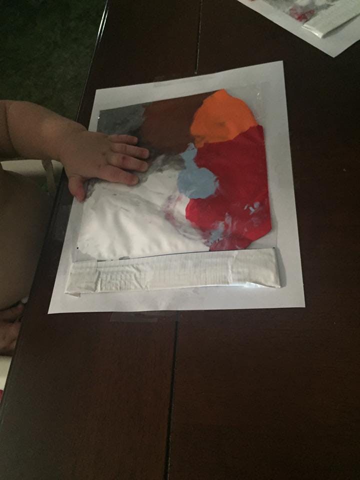 Child's hand on a plastic bag with paint inside colorful paint