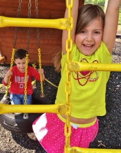 Child climbing on playground equipment, another child on a tire swing