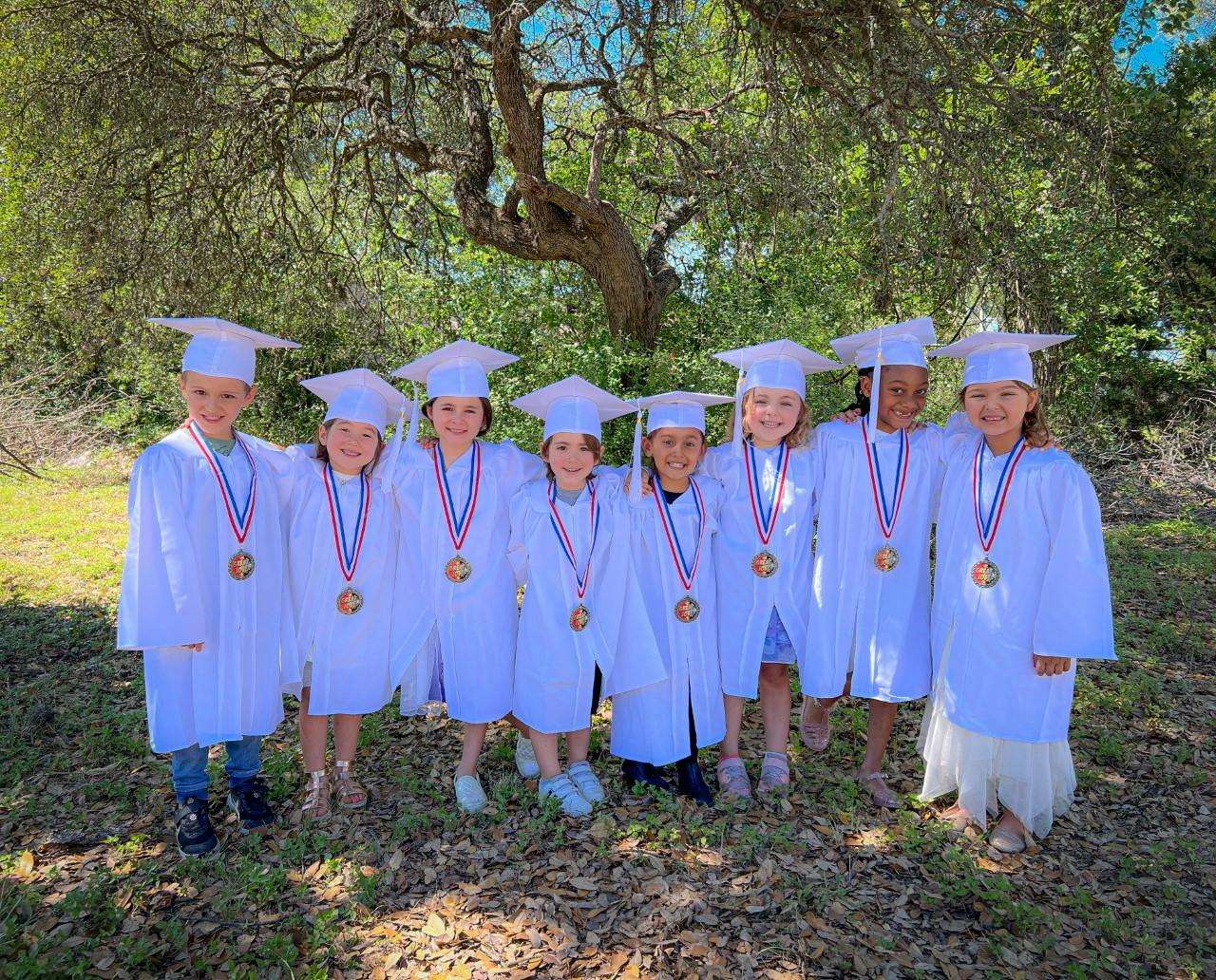 Group of children in white graduation caps and gowns with medals