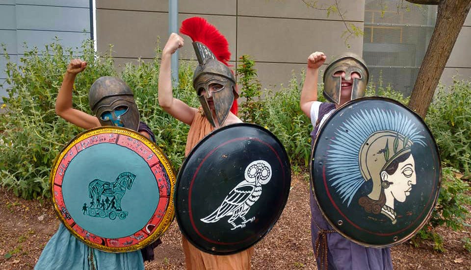 Three people in ancient Greek warrior helmets and tunics, holding shields