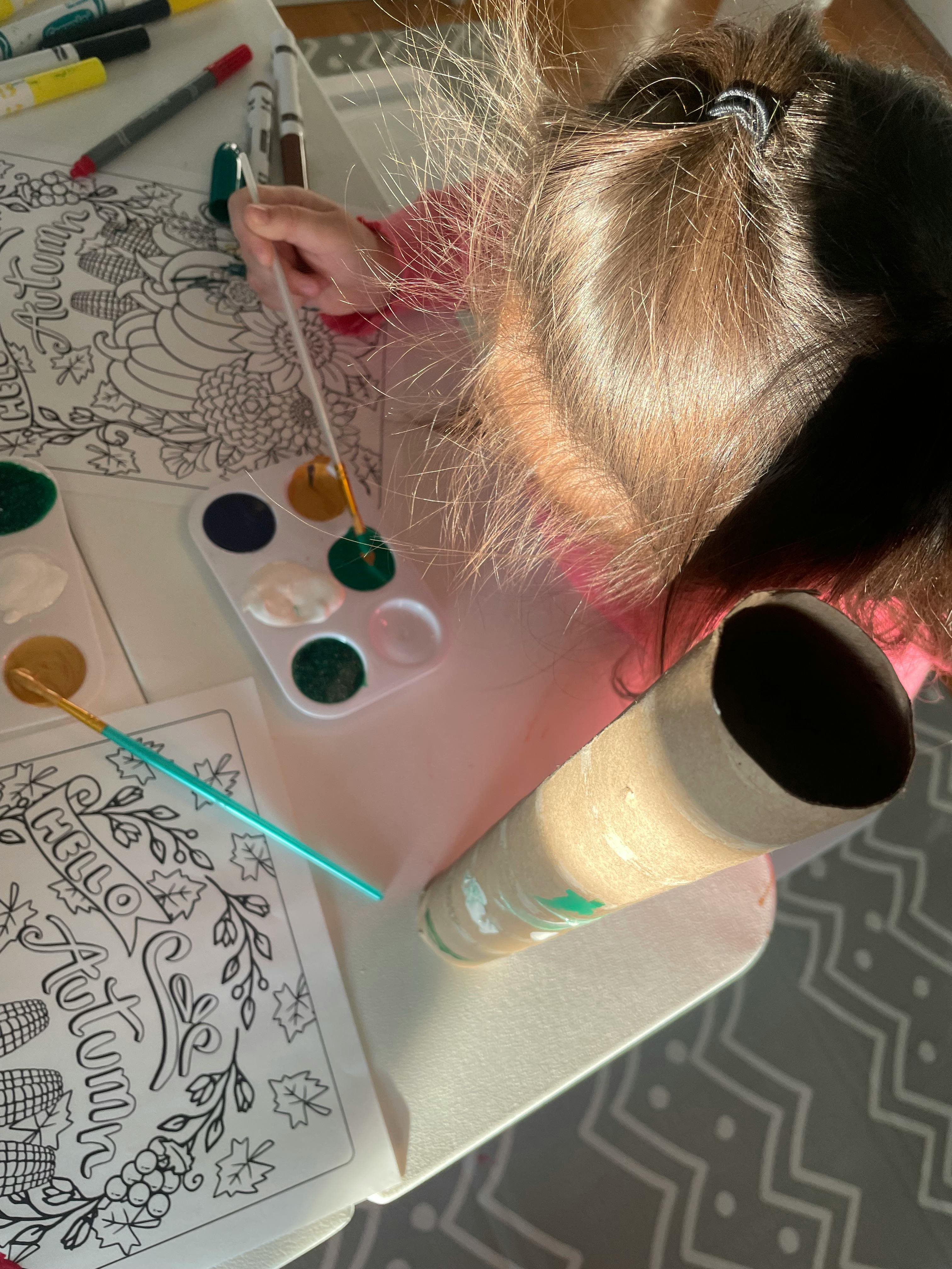 Child painting a coloring page with a paintbrush and paint palette