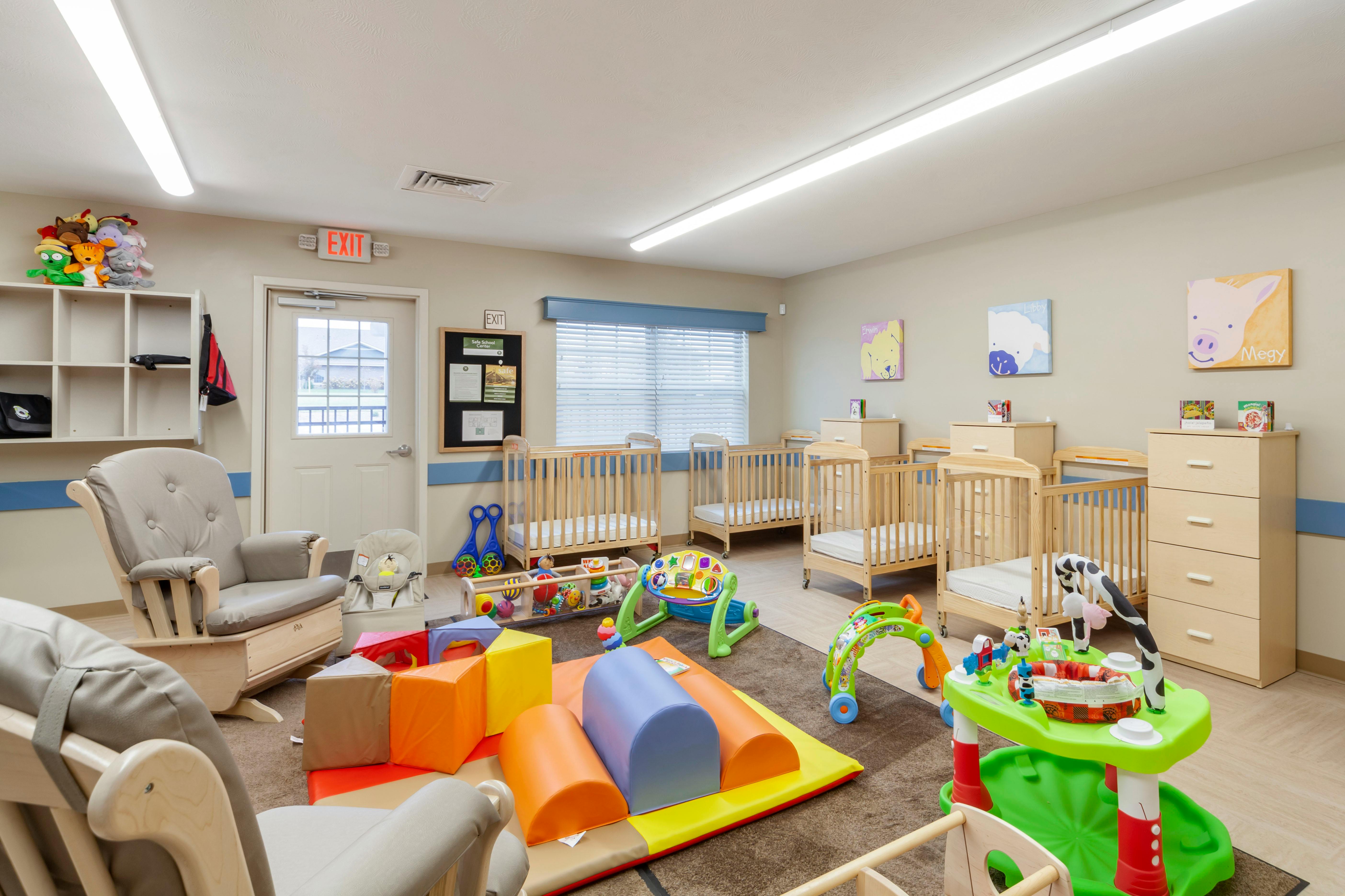 A room with several cribs, child play mats, toys, and two glider chairs