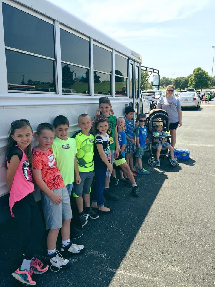Group of children and one adult standing next to a bus
