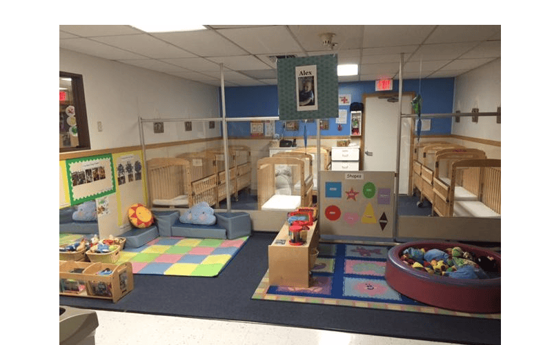 An empty nursery room with cribs, play mats, and a shape board