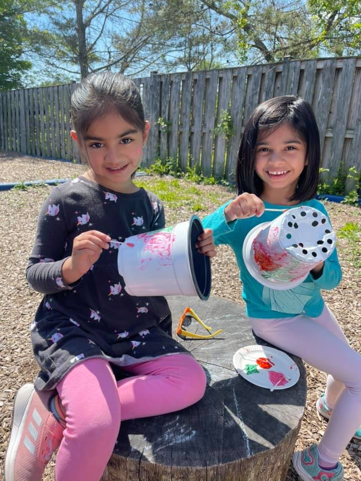 Two children painting flower pots outdoors