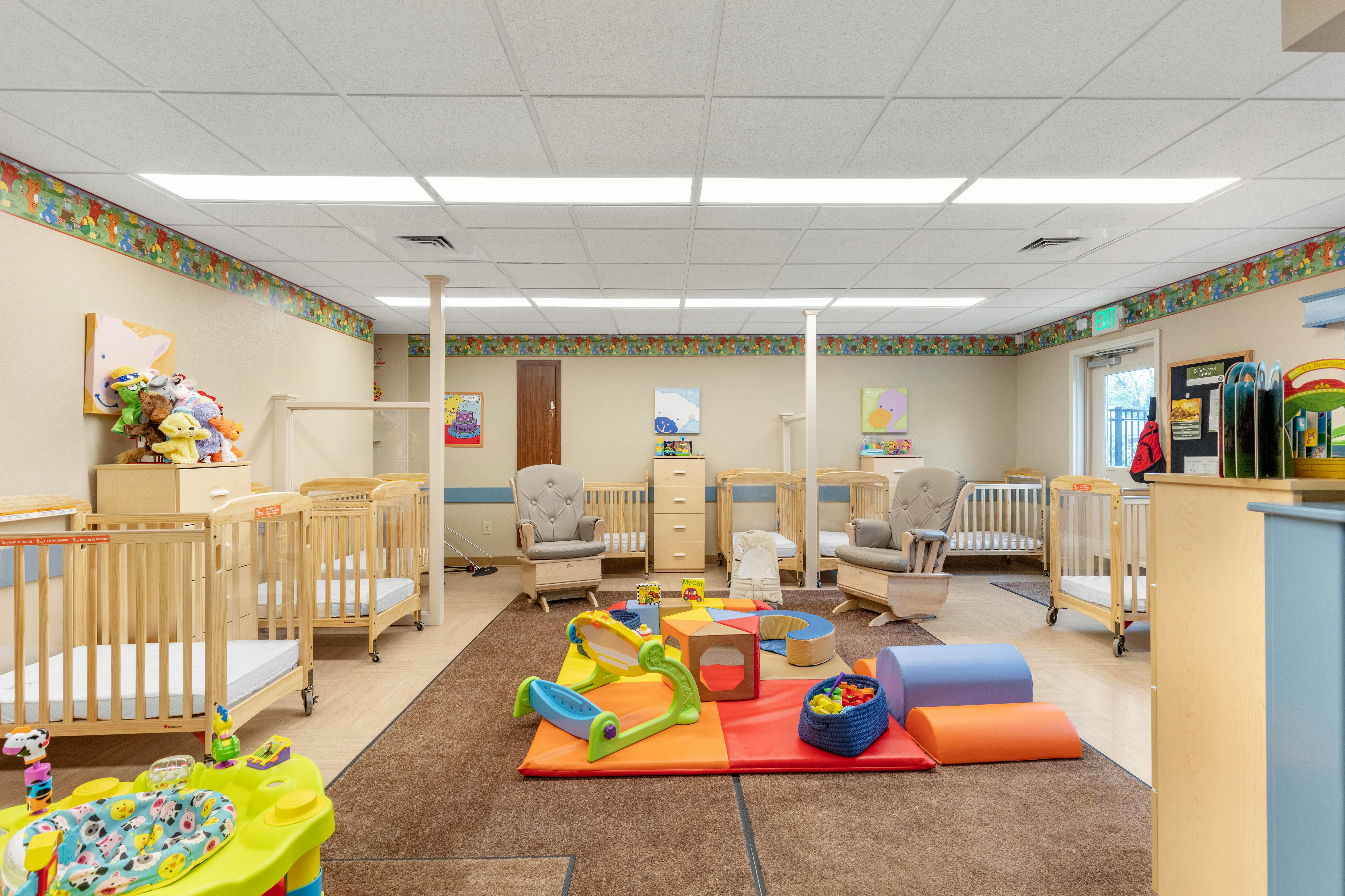 Baby room with multiple cribs, a rocking chair, and play mats with toys