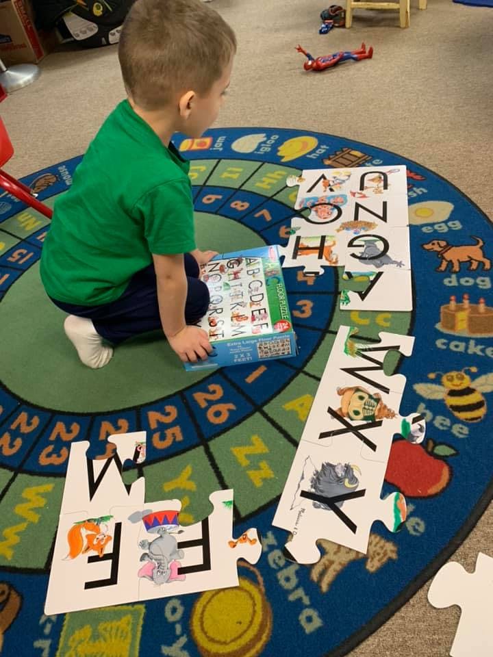 Child playing with alphabet puzzle pieces on a rug