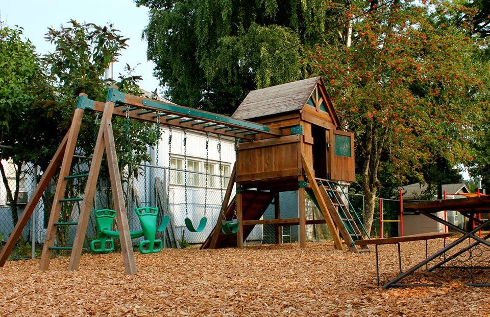 Playground with a wooden playhouse, swings, and monkey bars