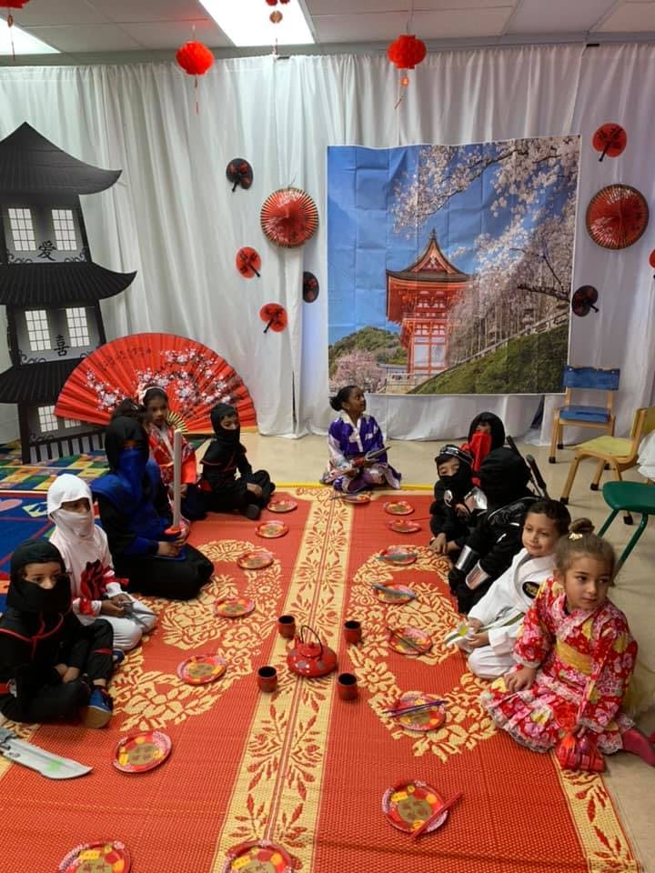 Children sitting on a red mat in a room decorated with Japanese-themed items