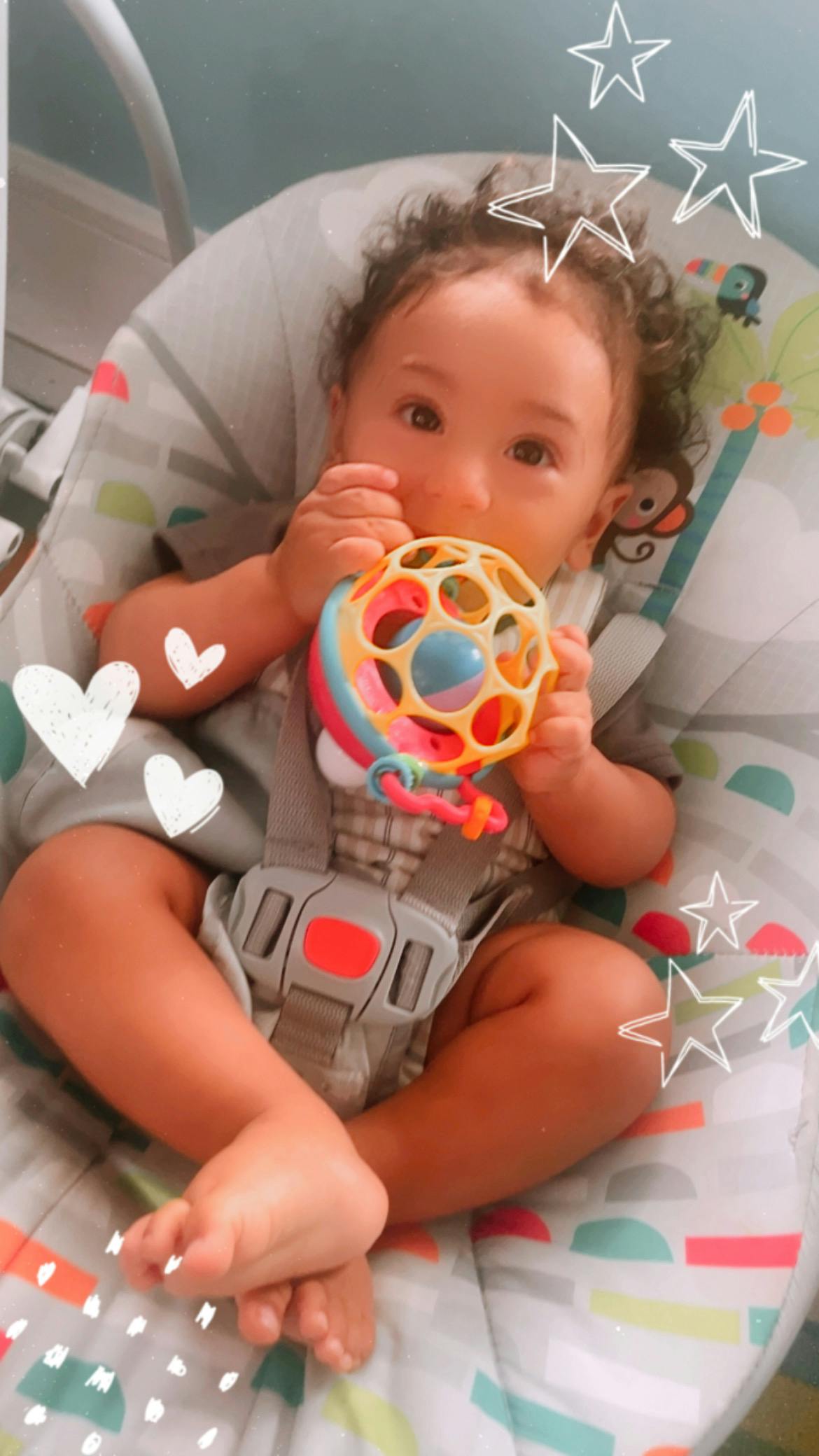 Child in a bouncer holding a colorful toy
