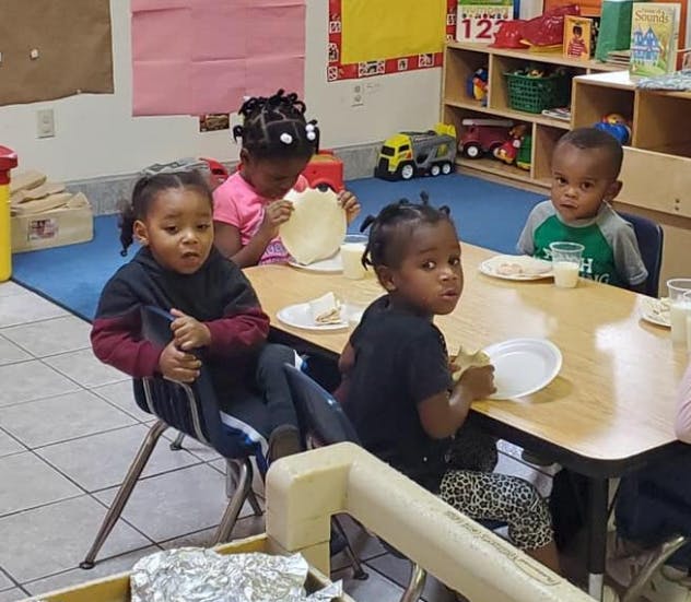 Four children sitting at a table eating in a classroom eating