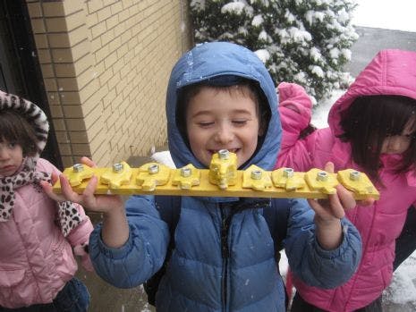 Child in blue coat holding a yellow menorah-like object with other children