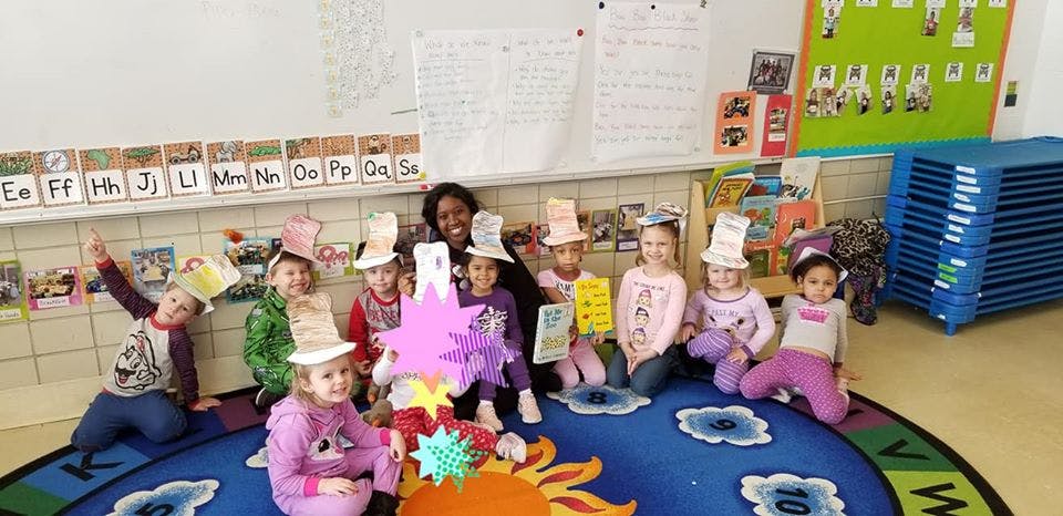Adult and children wearing paper hats sitting on a rug in a classroom