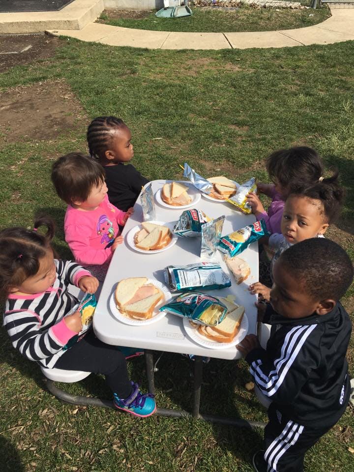 Children eating sandwiches and snacks at a table outdoors