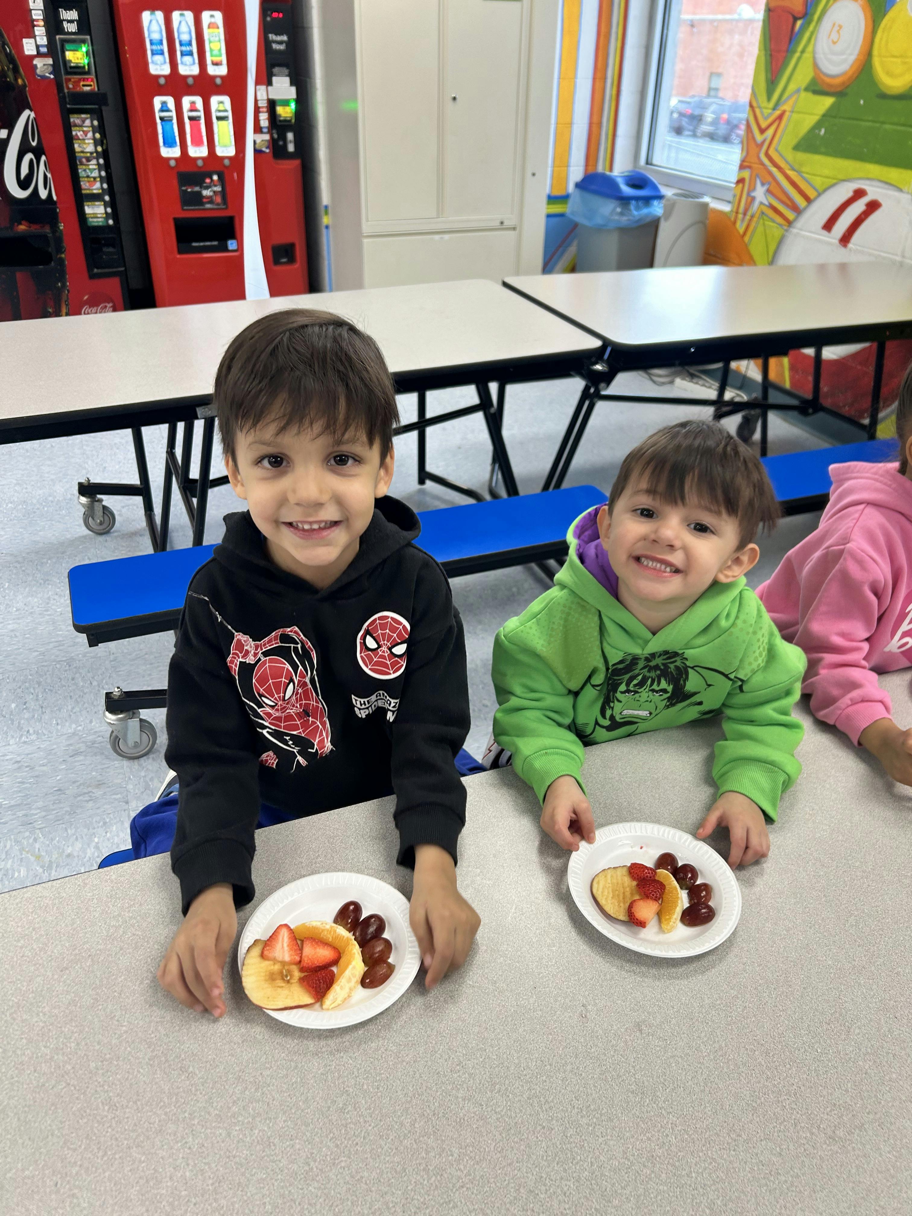 Two children sitting at a table with plates of fruit
