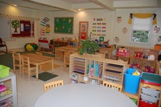Classroom with small tables and chairs, shelves with books and toys