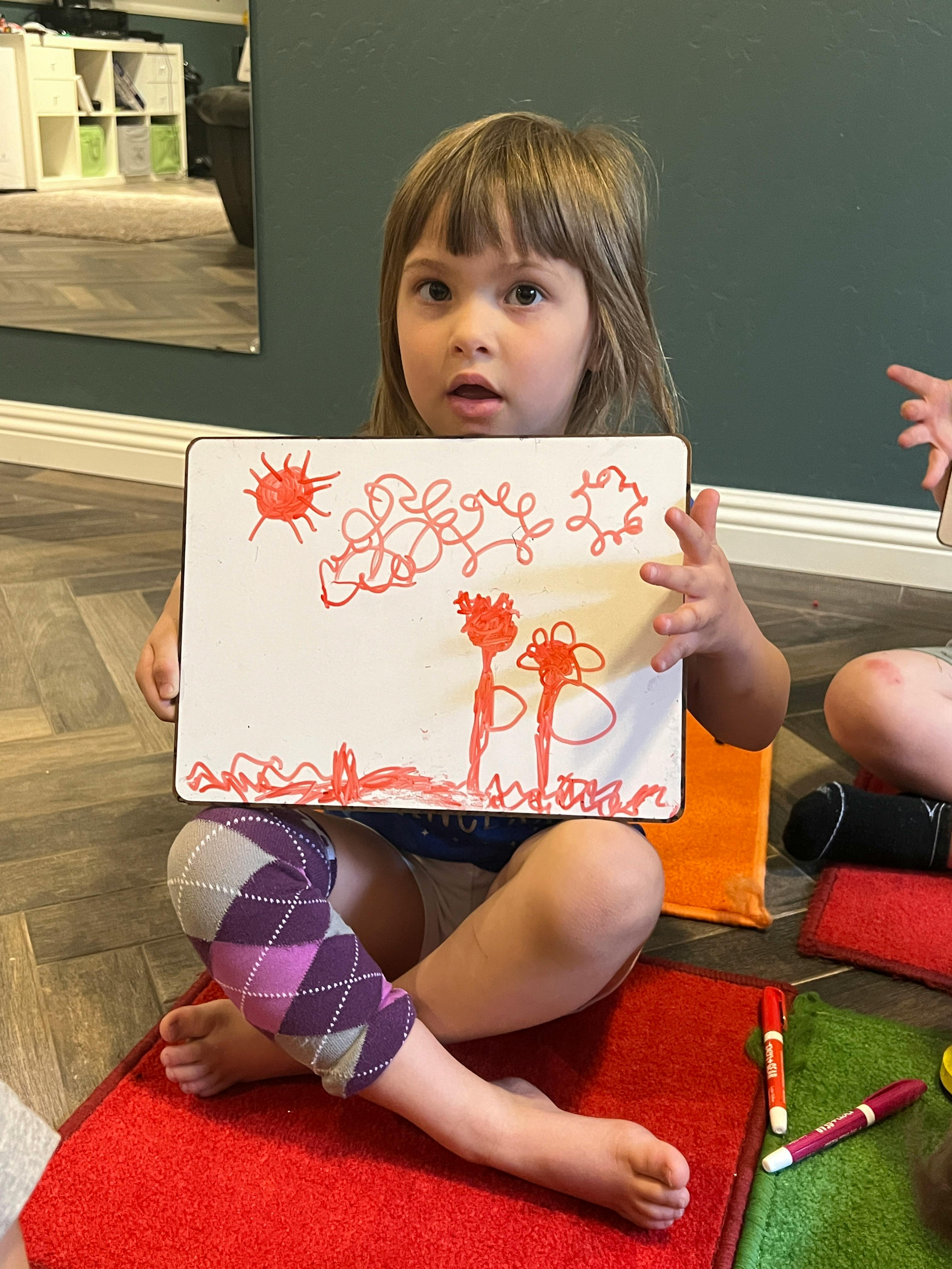 Child holding up a drawing on a whiteboard