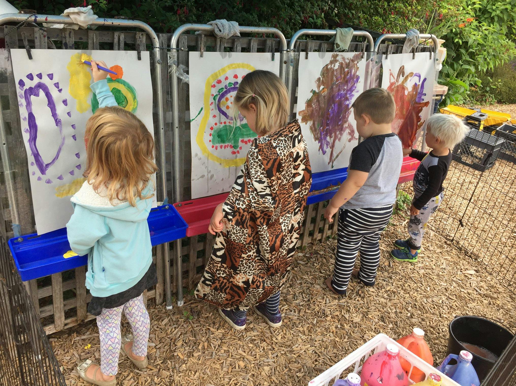 Four children painting on easels outdoors