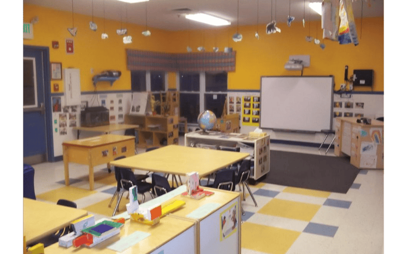 An empty classroom with yellow and blue walls and several tables and chairs