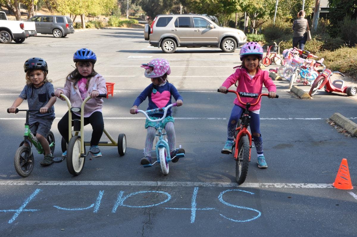 Four children on bikes and a tricycle at a start line drawn in chalk