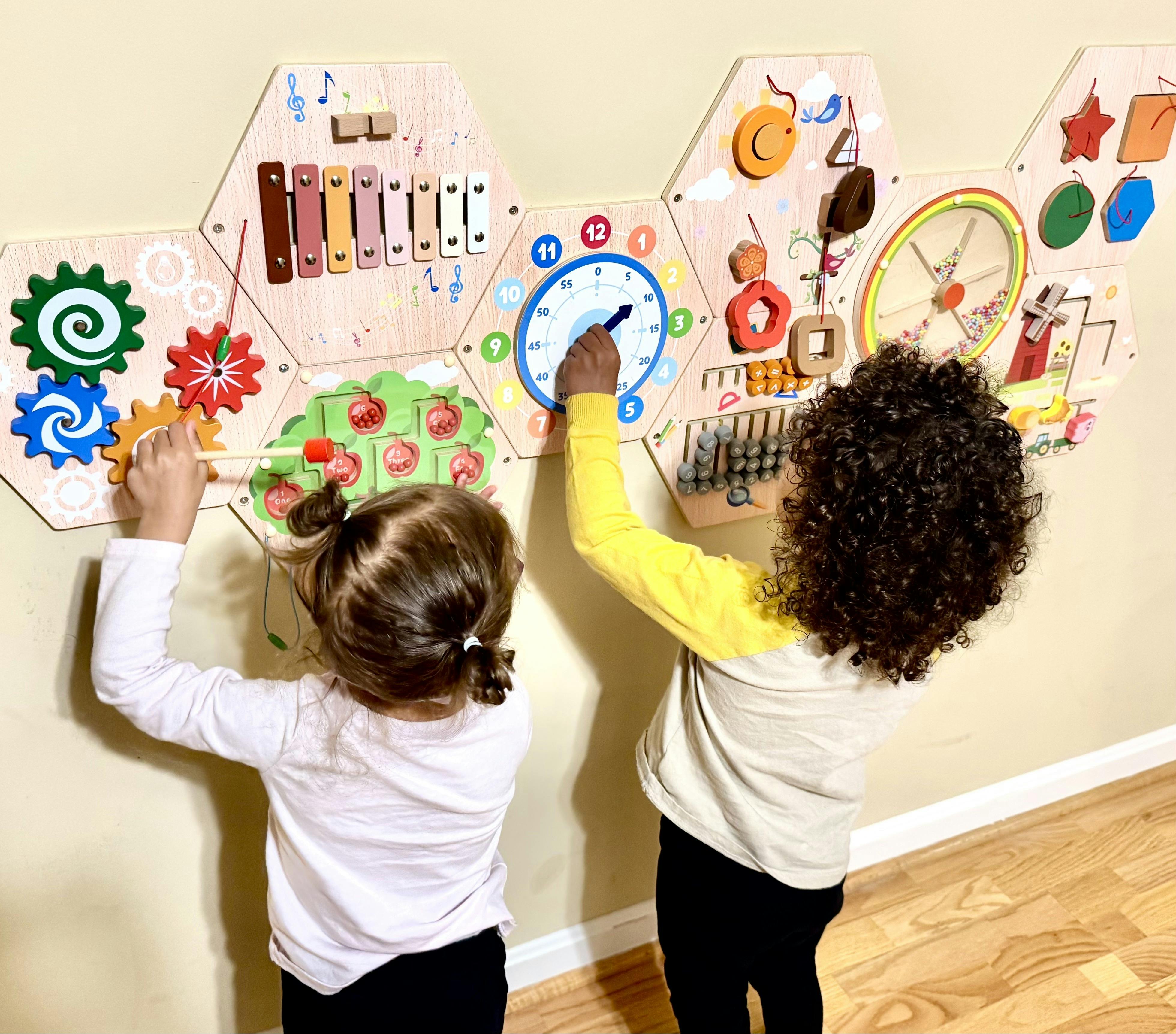 Two children playing with an interactive wooden activity wall board