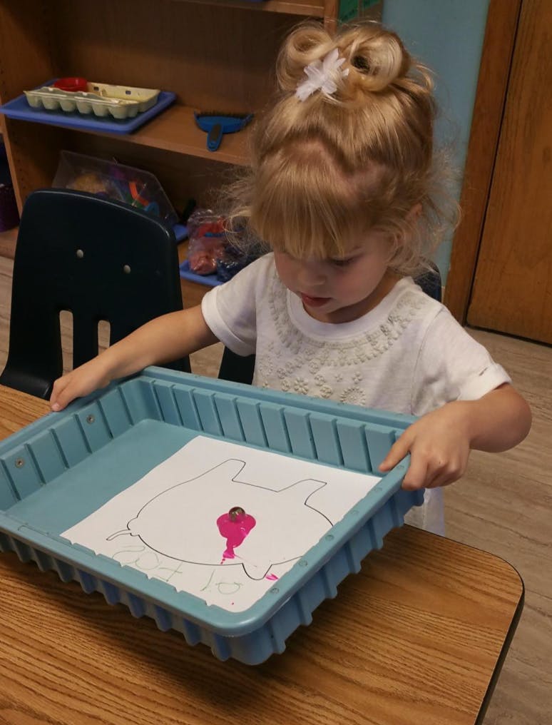 Child coloring a drawing in a blue tray