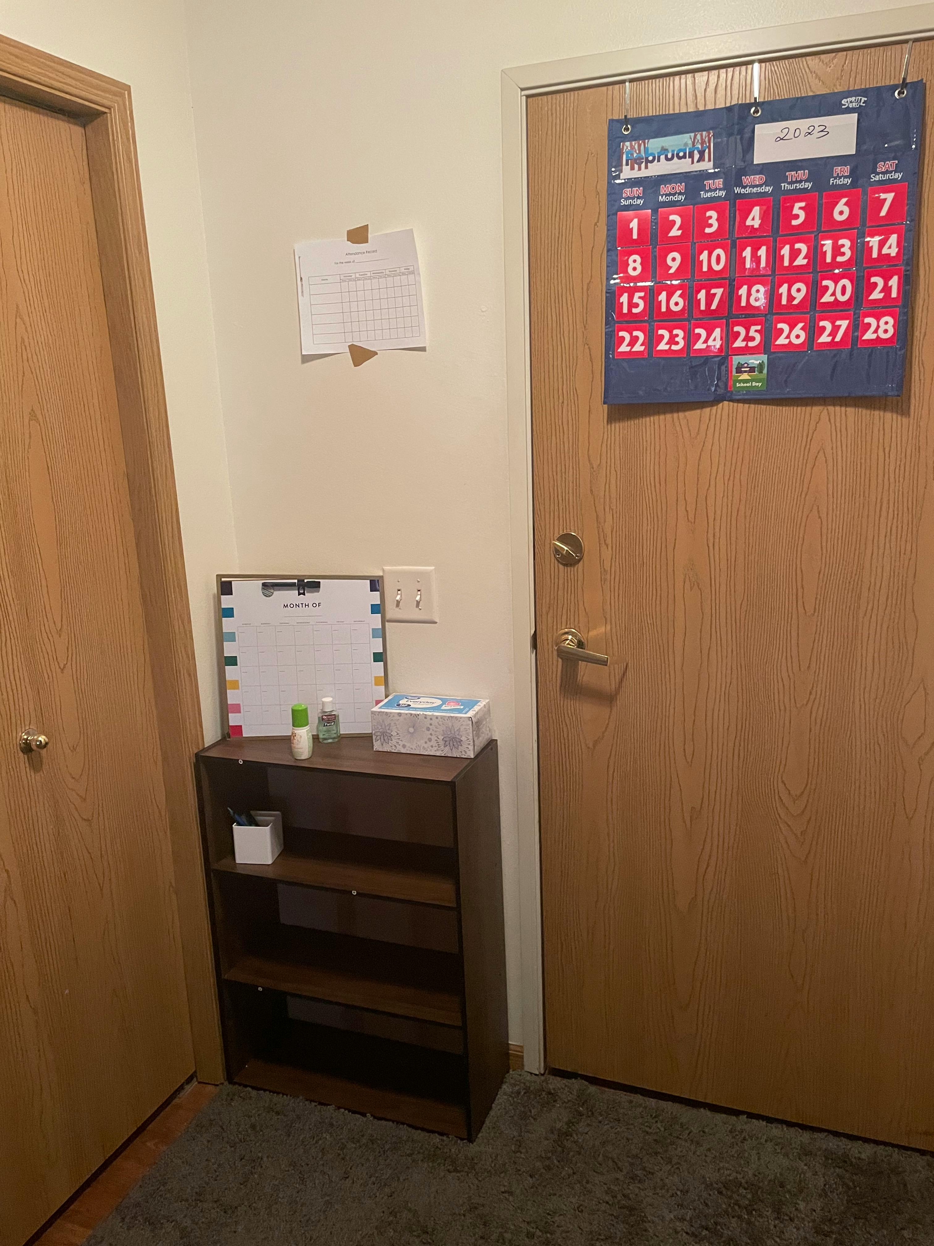 Wall with a calendar on a door and a small bookshelf
