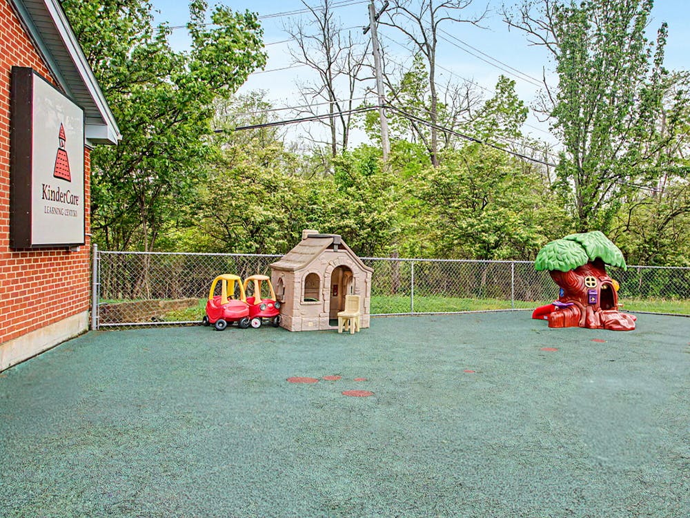 A playground with playhouses and cars on green rubber flooring