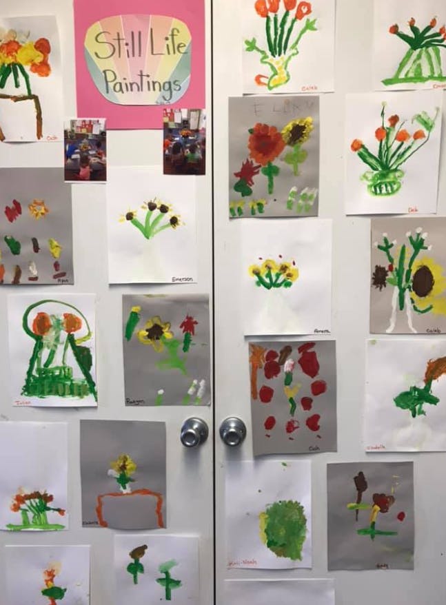 Children's still life paintings of flowers displayed on a wall