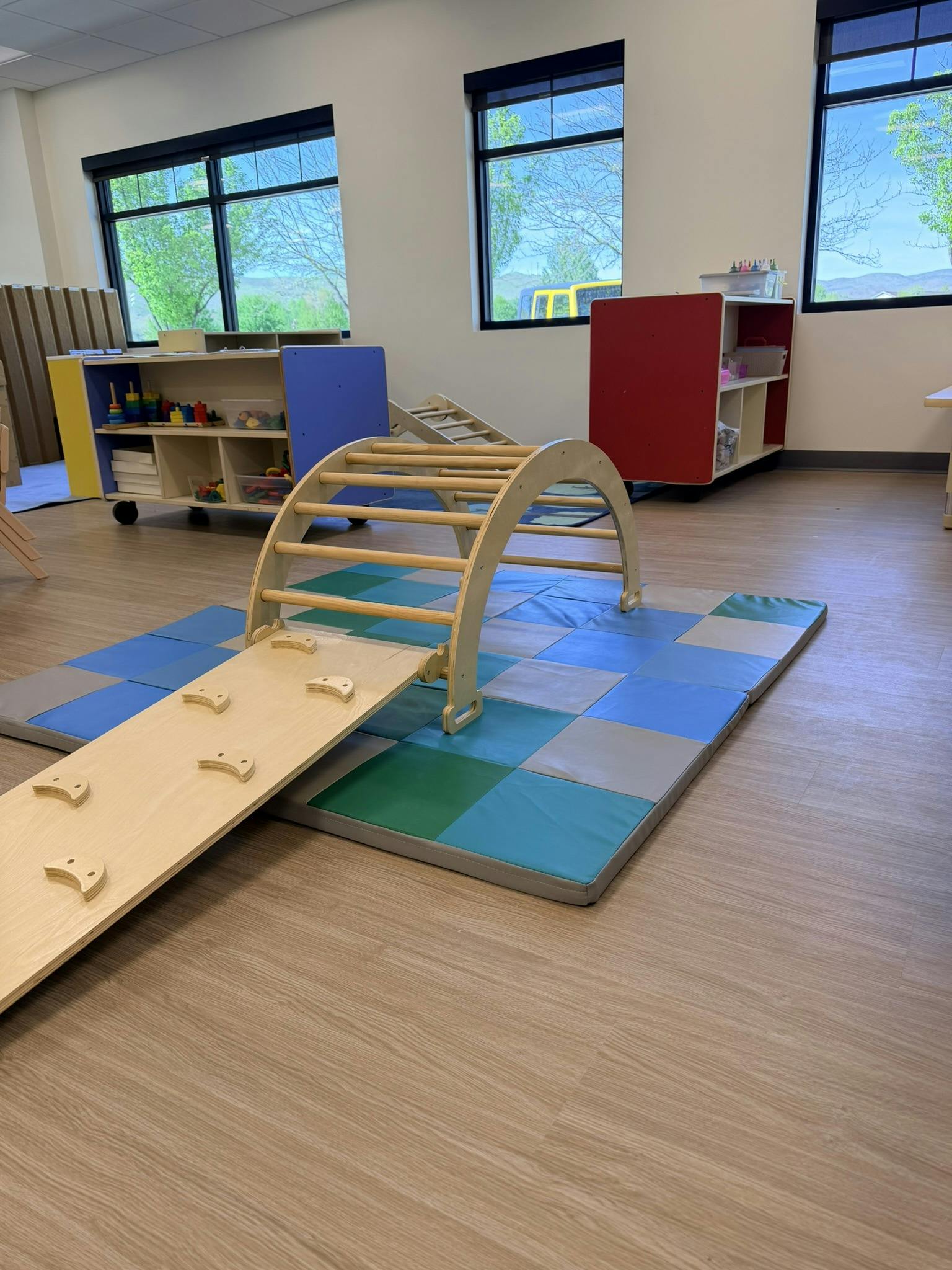 Wooden climbing arch with a ramp on blue and green mats in a room