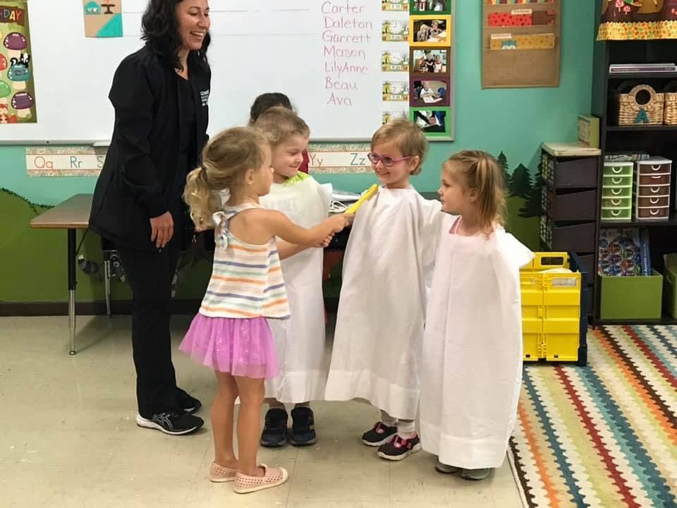 Adult and children in a classroom, some children wearing white smocks