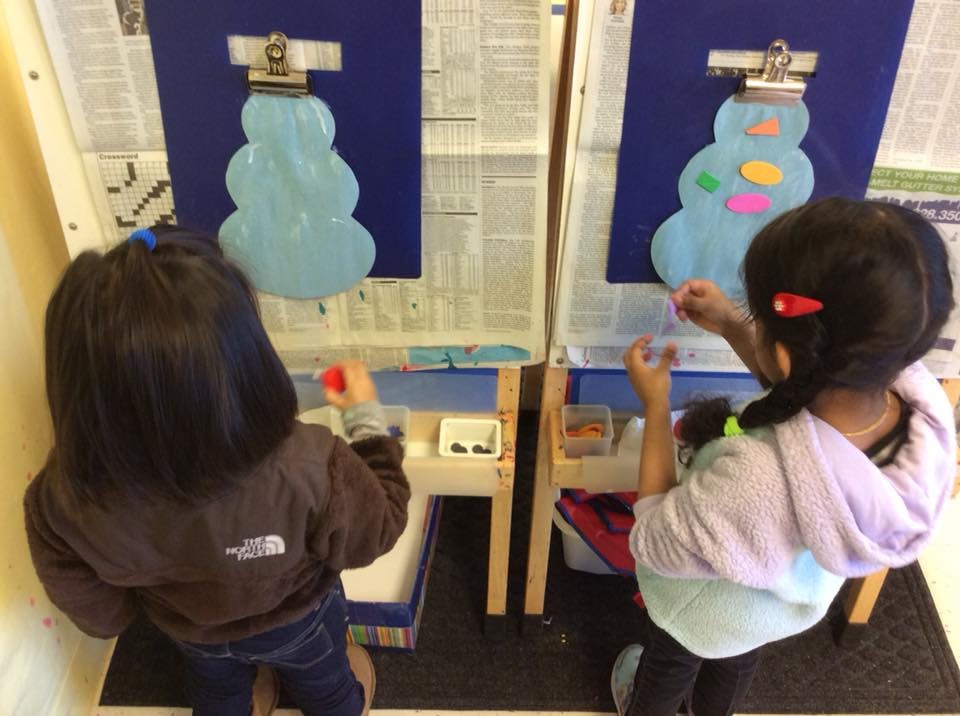 Two children decorating snowman cutouts on easels