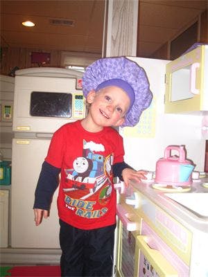 Child in a purple shower cap and red shirt standing in a play kitchen