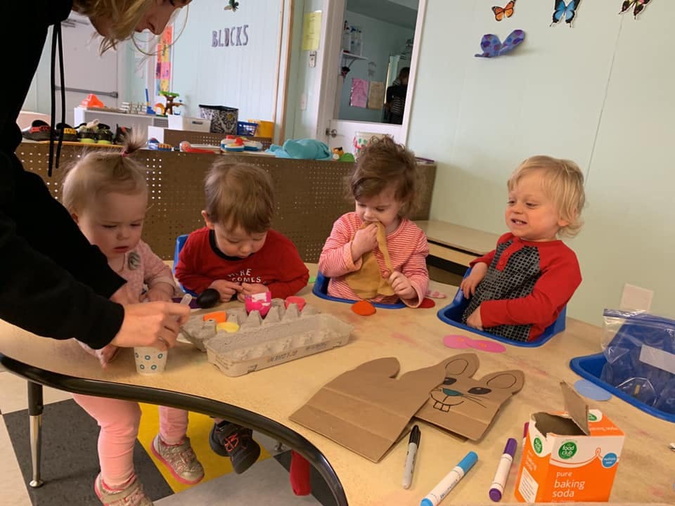 Adult helping children at a table with crafts