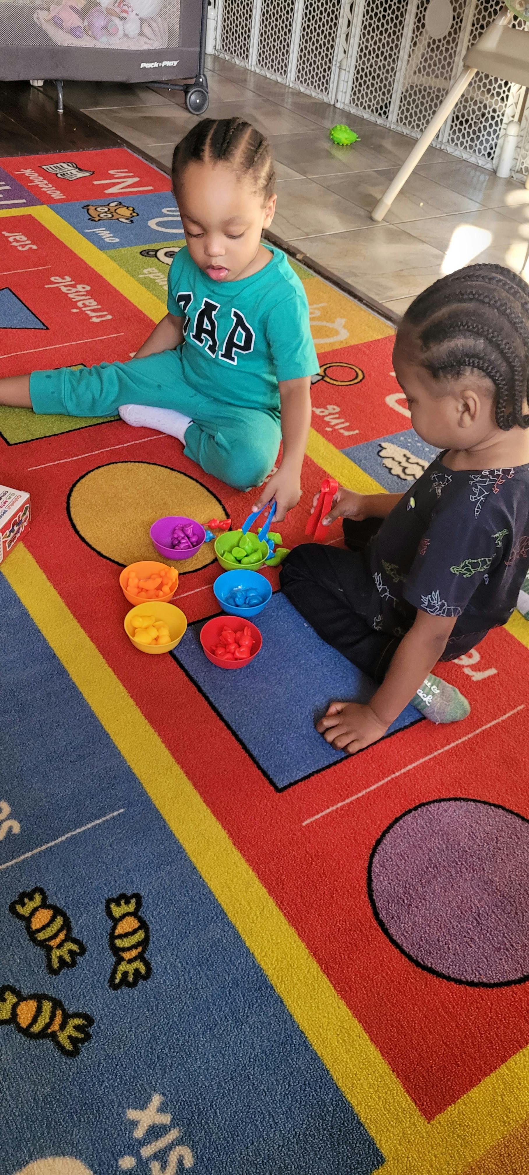 Two children playing with colorful bowls and small objects on a rug