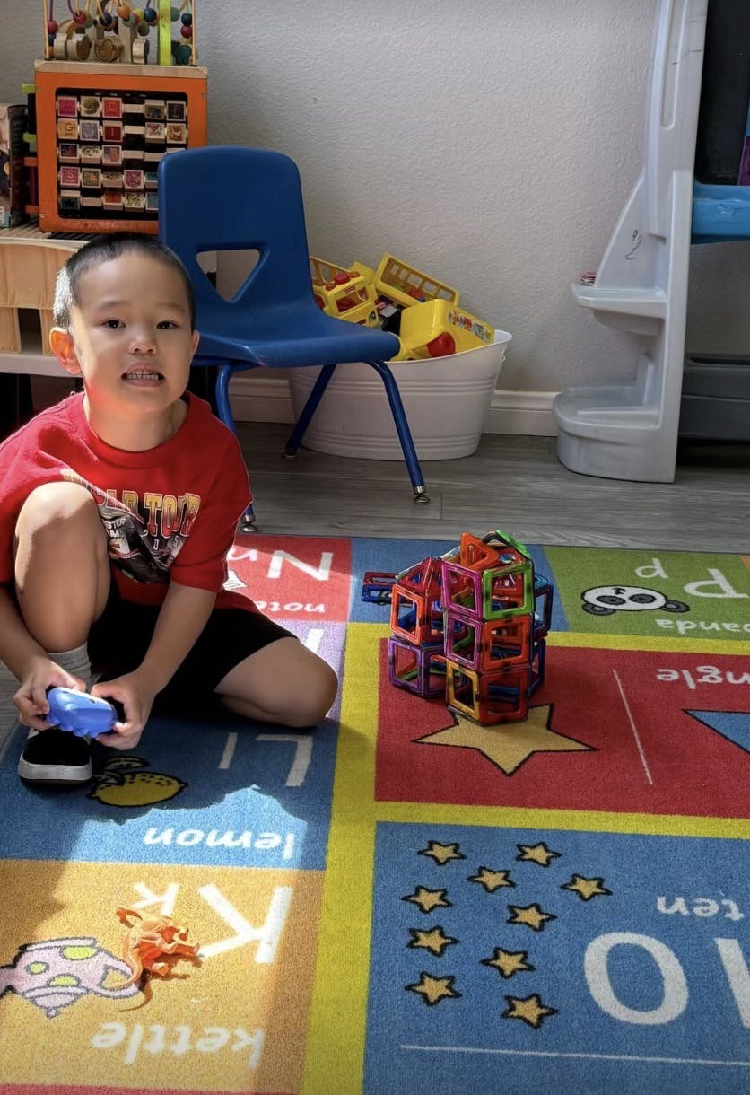 Child kneeling on a colorful rug, holding a blue toy