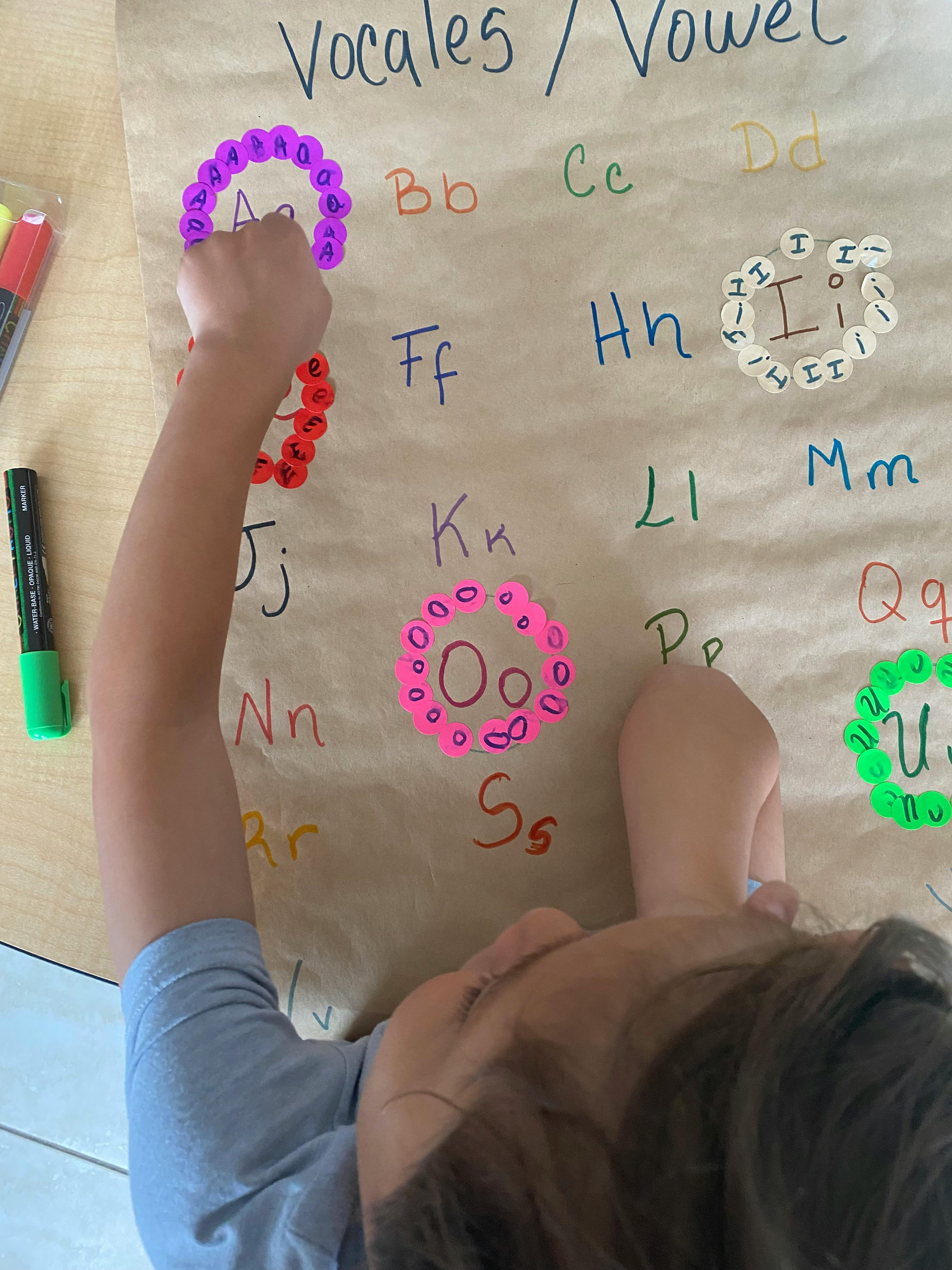 Child placing a sticker on a large brown paper with letters and words