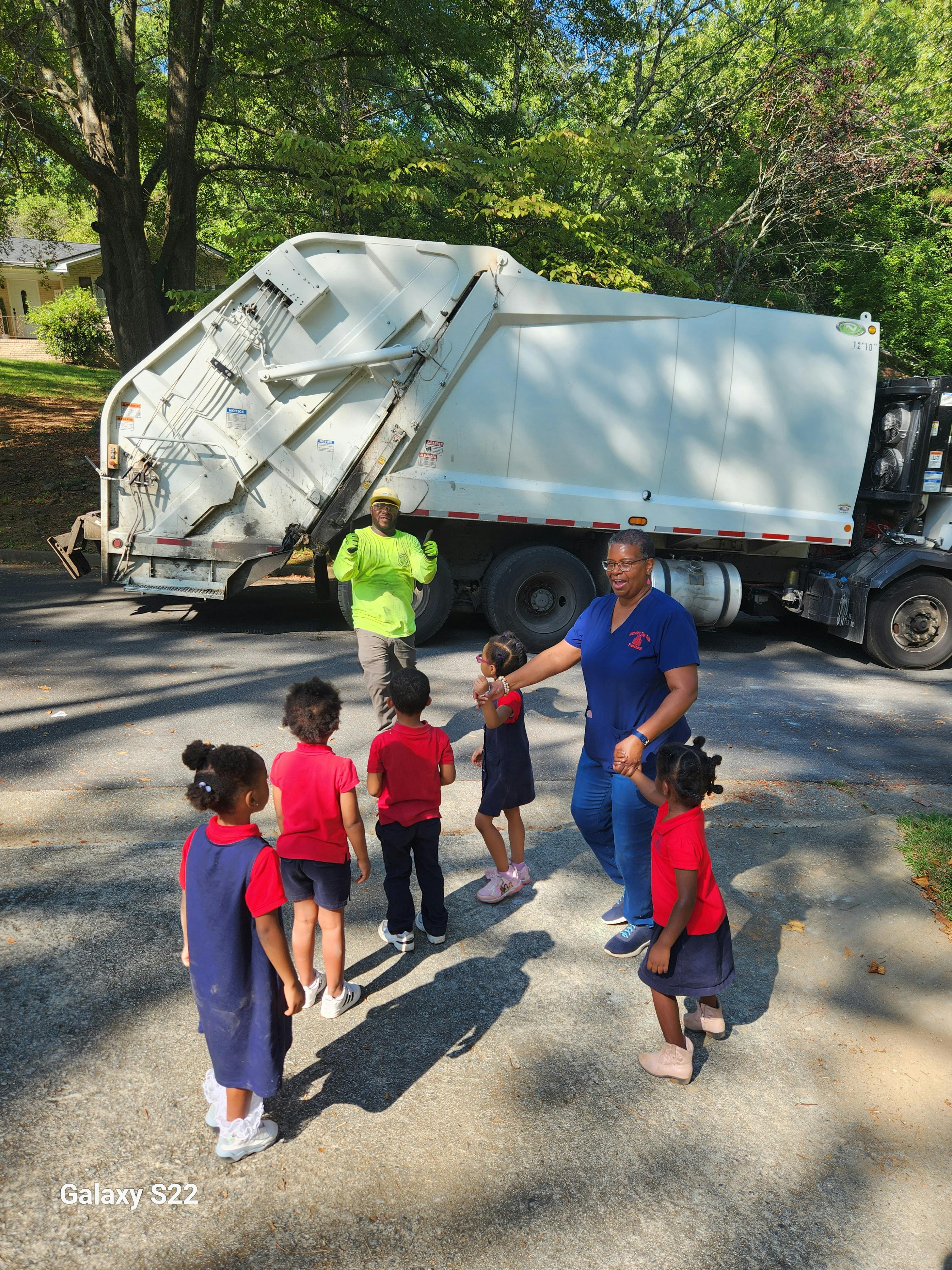 Adults and children standing near a garbage truck