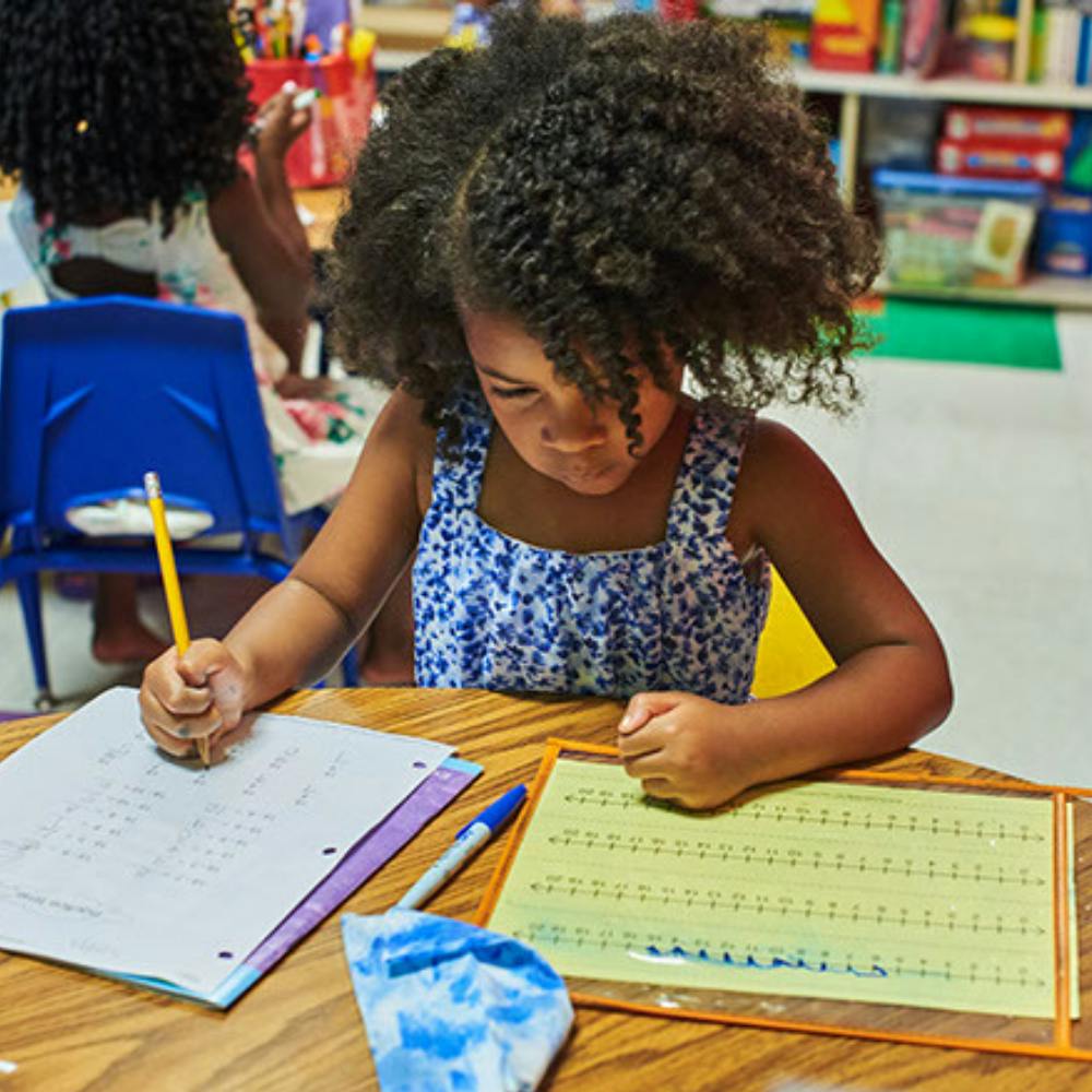 Child writing with a pencil at a desk in a classroom